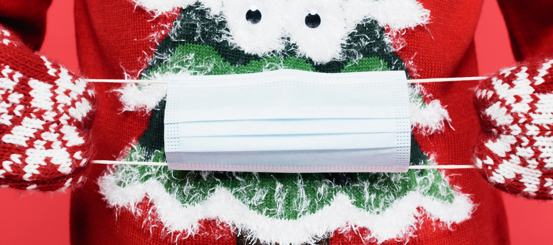 Closeup of disposable face mask stretched over holiday sweater of a Christmas tree.
